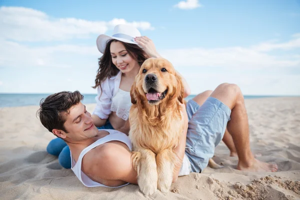Casal apaixonado brincando com seu cão na praia — Fotografia de Stock
