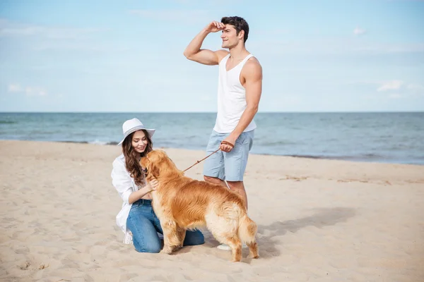 Casal apaixonado brincando com seu cão na praia — Fotografia de Stock