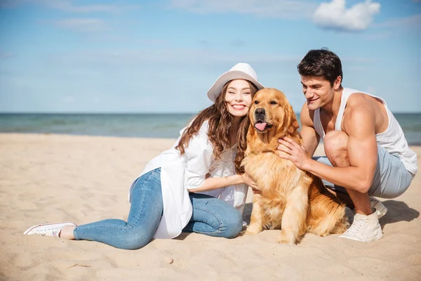 Giovane coppia innamorata seduta sulla spiaggia con cane — Foto Stock
