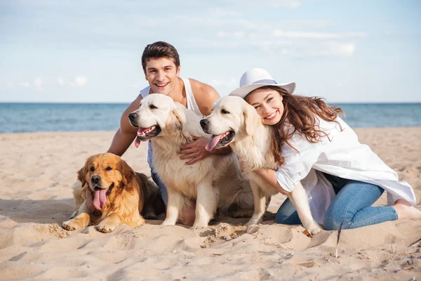 Casal abraçando três cães e sentado na praia — Fotografia de Stock