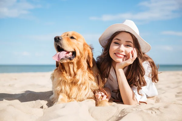 Vrolijke jonge vrouw liggend met haar hond op het strand — Stockfoto
