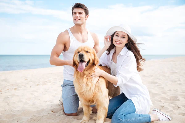 Glada unga par med hund sitter på stranden — Stockfoto
