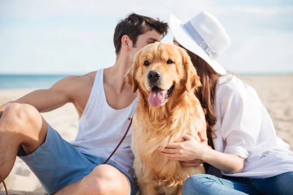 Paar sitzt am Strand und versteckt sich hinter dem Hund — Stockfoto