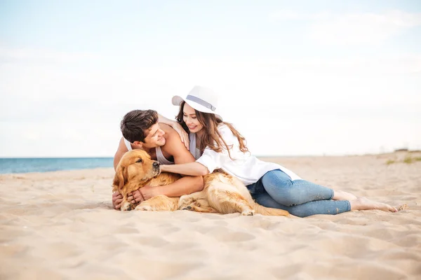 Giovane coppia attraente con un cane seduto sulla spiaggia — Foto Stock