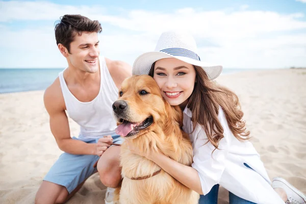 Bonito jovem casal abraçando um cão na praia — Fotografia de Stock