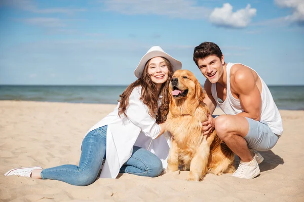 Feliz jovem casal se divertindo com o cão na praia — Fotografia de Stock