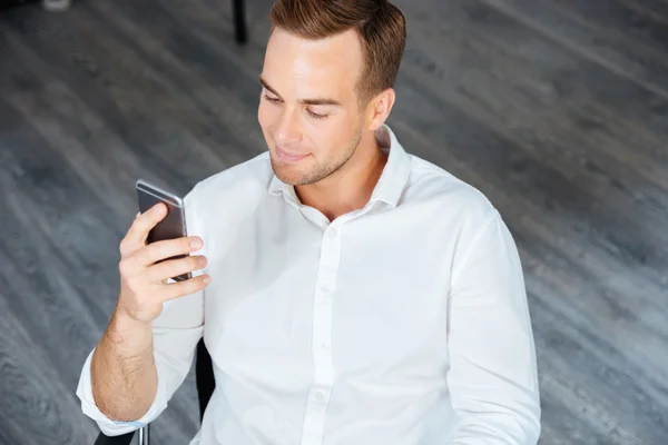 Empresário sentado e usando smartphone no escritório — Fotografia de Stock