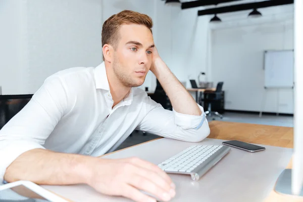 Sad bored young businessman working with computer in office — Stock Photo, Image