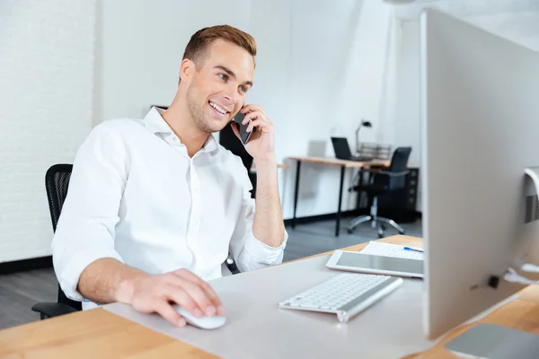 Smiling businessman working with computer and talking on cell phone