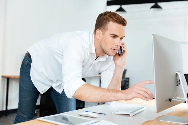 Homme d'affaires parlant sur téléphone portable et utilisant l'ordinateur dans le bureau — Photo