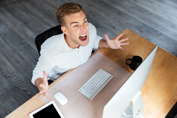 Irritierter junger Geschäftsmann arbeitet mit Computer und schreit — Stockfoto