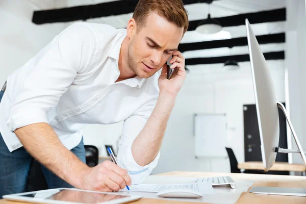 Businessman talking on cell phone and writing in office