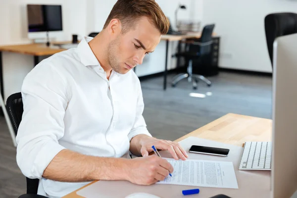 Affärsman sitter och underteckna dokument i office — Stockfoto