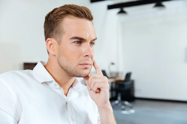 Pensive young businessman sitting and thinking in office — Stock Photo, Image
