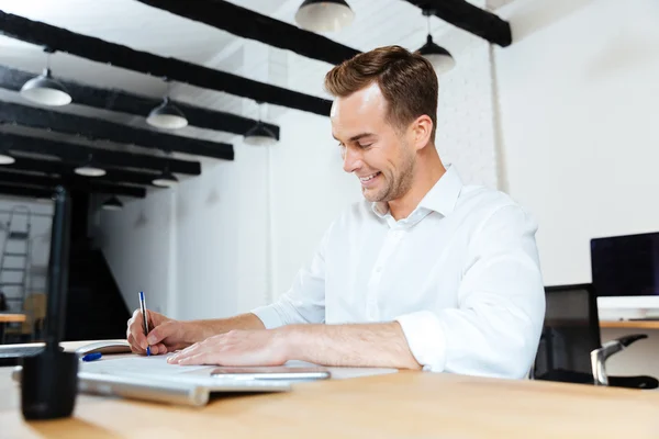 Happy businessman smiling and writing at the table — Stock Photo, Image