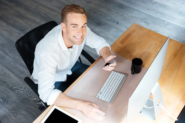 Happy businessman working with smartphone and computer in office — Stock Photo, Image