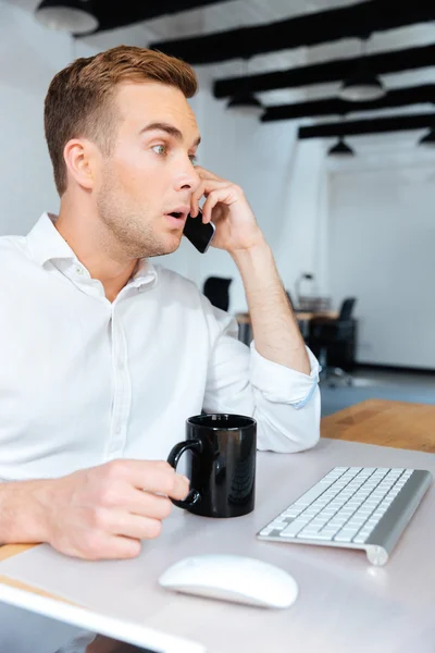 Удивительно удивленный бизнесмен разговаривает по телефону и пьет кофе — стоковое фото