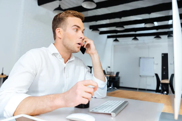 Sorprendido joven empresario bebiendo café y hablando por teléfono celular — Foto de Stock