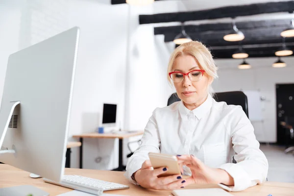 Schöne reife Frau mit Smartphone im Büro — Stockfoto