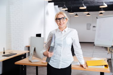 Ayakta ve klasörleri ofiste tutan mutlu işkadını