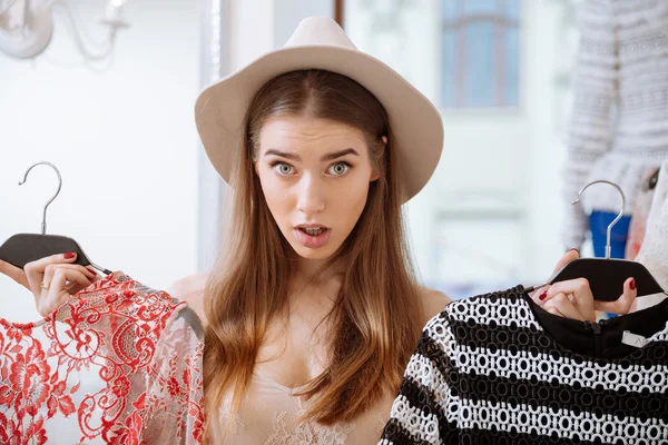 Puzzled young woman choosing clothes in clothing store — Stock Photo, Image