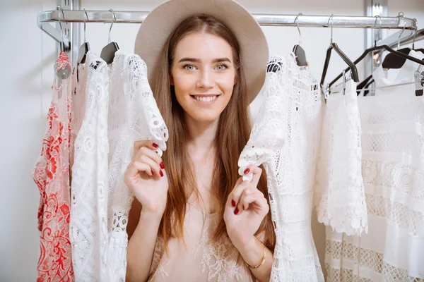 Happy pretty young woman choosing clothes in clothing store — Stock Photo, Image