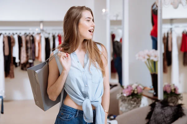 Mujer sorprendida sosteniendo bolsa de compras y de pie en la tienda de ropa — Foto de Stock