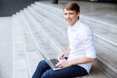 Merdivenlerde oturan ve dizüstü bilgisayar açık havada kullanarak adam gülümseyen