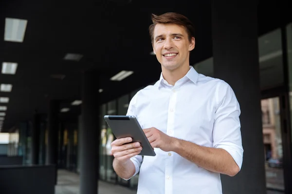 Hombre de negocios sonriente de pie y utilizando la tableta cerca del centro de negocios — Foto de Stock