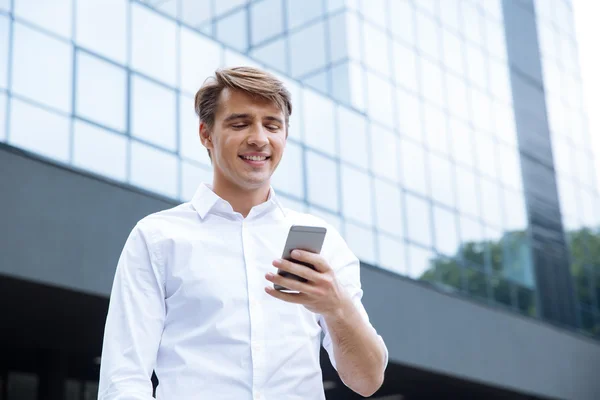 Mosolygó fiatal üzletember üzleti központ közelében mobiltelefon használata — Stock Fotó