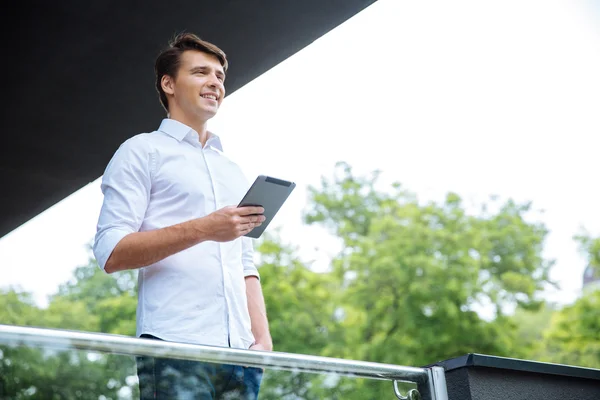 Feliz hombre de negocios de pie en el balcón y utilizando la tableta — Foto de Stock