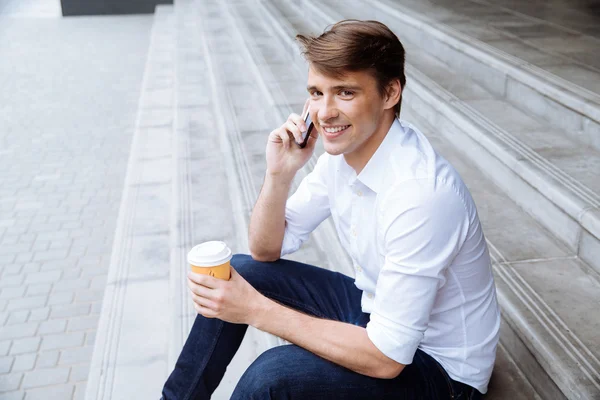 Smiling businessman drinking coffee and talking on cell phone — Stock Photo, Image