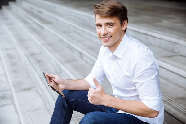 Hombre de negocios alegre sentado y usando la tableta al aire libre — Foto de Stock