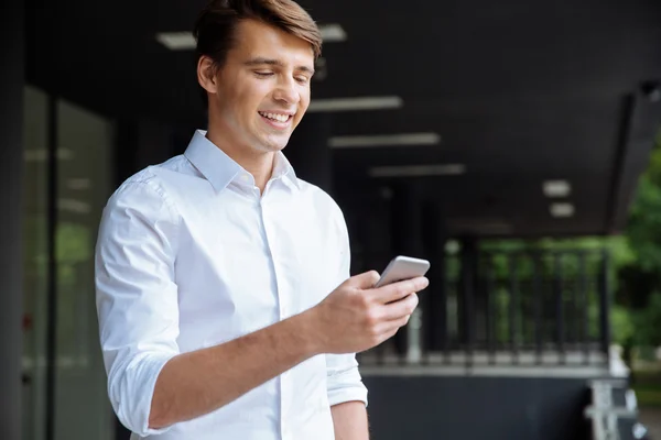 Hombre de negocios feliz usando smartphone y sonriendo cerca del centro de negocios — Foto de Stock