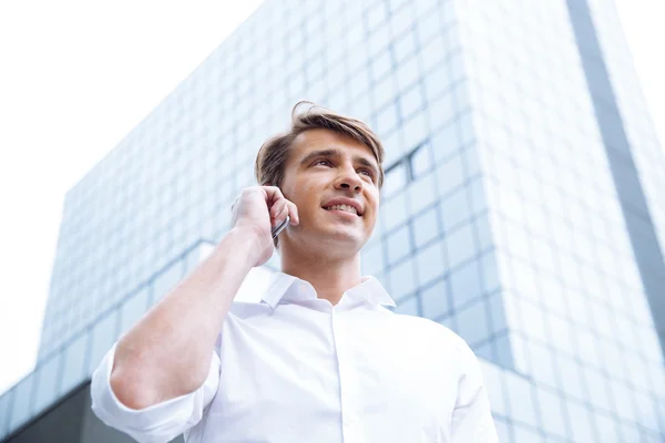 Empresario pisando rascacielos y hablando por celular — Foto de Stock