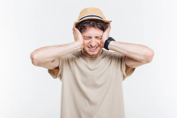 Frowning young man covered ears with hands over white background — Stock Photo, Image