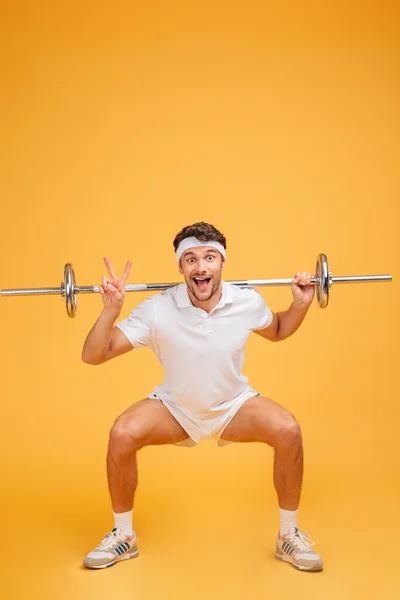 Drôle sportif faire squats avec haltère et montrant signe de paix — Photo