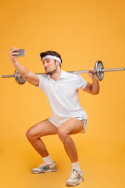 Komik sporcu barbell ile egzersiz ve akıllı telefon kullanarak selfie konuşan — Stok fotoğraf