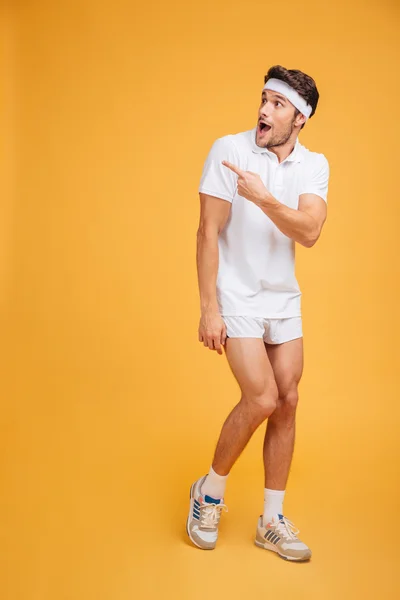 Surprised young man athlete with opened mouth pointing away — Stock Photo, Image