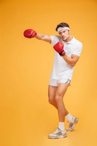Forte jovem boxeador em luvas vermelhas de pé e lutando — Fotografia de Stock