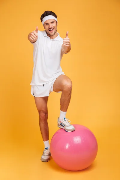 Fitness topu üzerinde bir ayak ile Sportman başparmak gösteren — Stok fotoğraf
