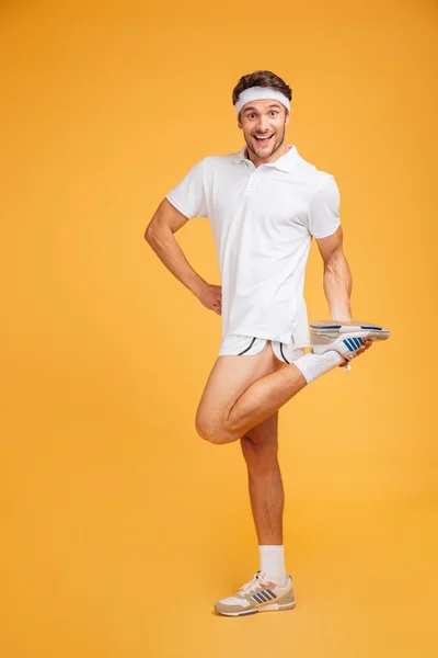 Cheerful young sportsman standing and stretching legs — Stock Photo, Image