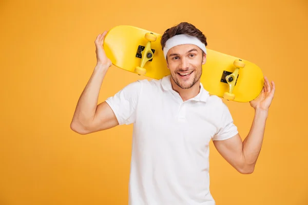 Joven patinador alegre sosteniendo un monopatín sobre sus hombros — Foto de Stock