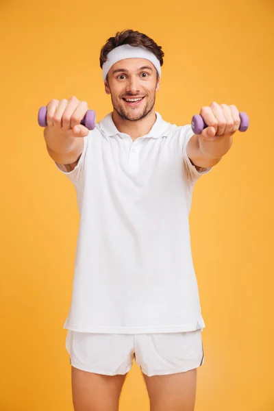 Happy young man athlete standing and working out with dumbbells — Stock Photo, Image