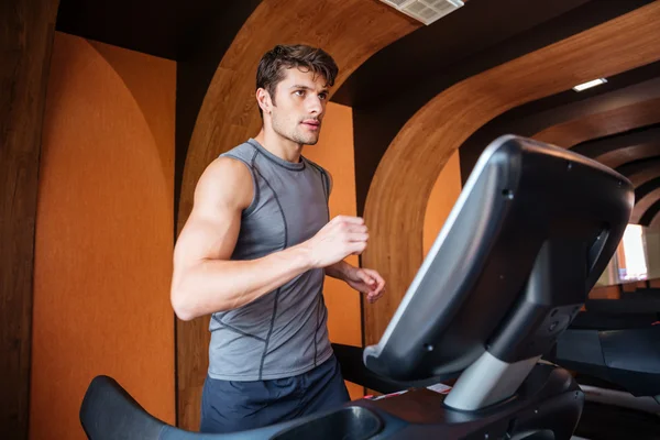 Jeune homme en vêtements de sport courir sur tapis roulant à la salle de gym — Photo