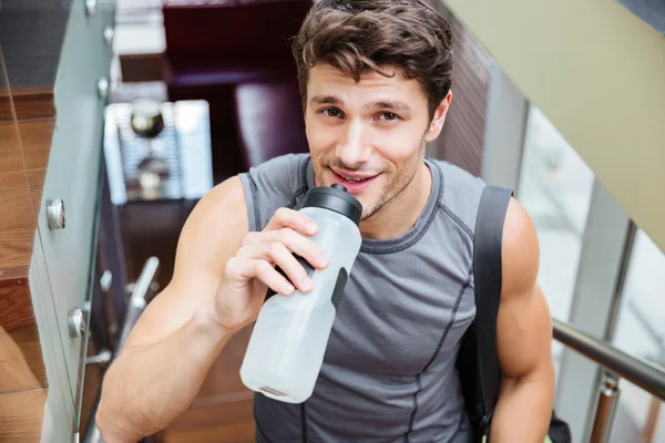 Ein lächelnder Sportler geht und trinkt Wasser in der Turnhalle — Stockfoto