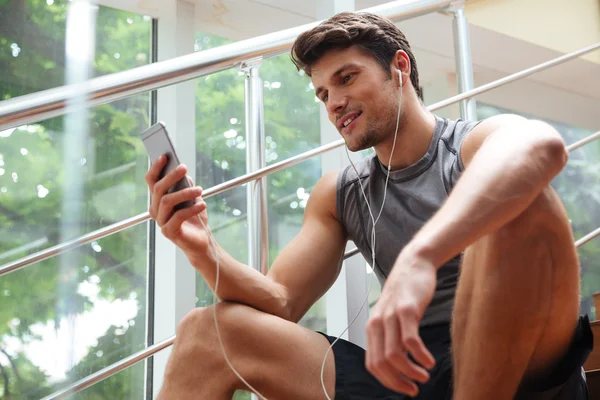 Sportler sitzt und hört Musik vom Smartphone — Stockfoto