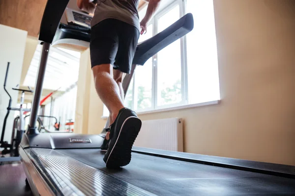 Legs of young man athlete running on treadmill in gym — Stock Photo, Image