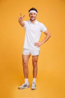 Ayakta ve zafer işaret gösteren mutlu yakışıklı genç erkek atlet