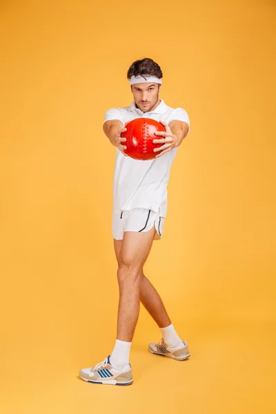 Comprimento total do homem esportivo sério exercitando com bola vermelha — Fotografia de Stock